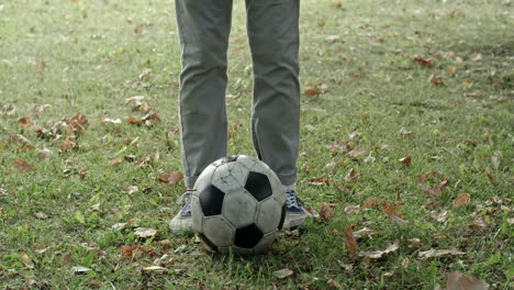 boy in blue cap and plaid shirt bends down to catch soccer ball in park and looks at camera