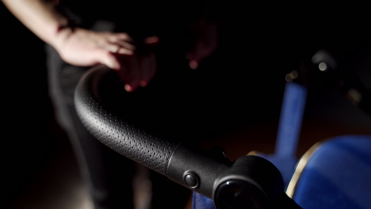 Black handle of a baby stroller. Woman runs her hand over the handler of a pram. Close up. Blurred backdrop.