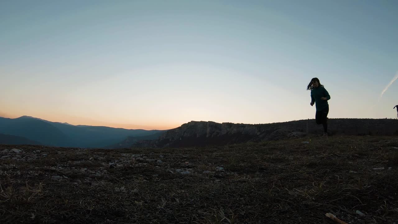 niña corriendo con un perro labradot negro en una montaña al atardecer durante el otoño