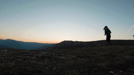 Young-girl-running-with-a-black-labradot-dog-on-a-mountain-at-sunset-during-autumn