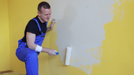 man making repairs in new flat. young man painting wall with roller brush while renovating his apartment