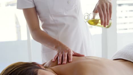 masseur pouring massage oil on the back of her patient