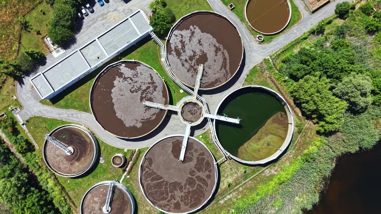 Planta de tratamiento de aguas residuales en funcionamiento con múltiples tanques y diferentes colores de agua en un diseño estructurado.
