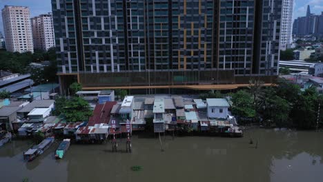 Aerial-view-on-Kenh-Te-canal-Ho-Chi-Minh-City-with-old-iron-and-wood-shacks,-traditional-river-boats-and-ultra-modern-high-rise-buildings-on-sunny-day