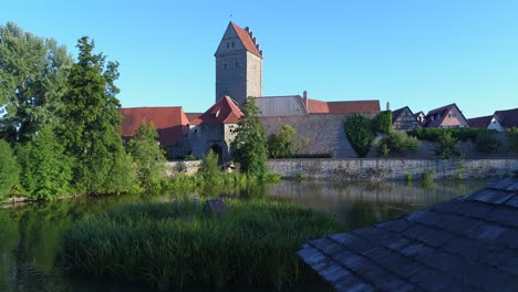 drone flies slowly forward passes a gazebo continues on the lake in front is the tower gate wall and some roofs of an old historic city