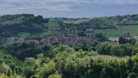 castell'arquato, a medieval village in emilia romagna, stands out among the green hills of piacenza, surrounded by lush vegetation and vineyards, under a cloudy sky promising rain