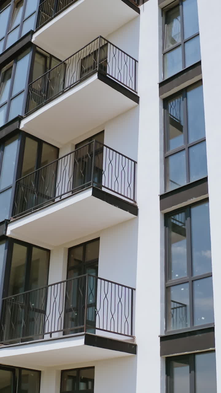 Block of flats on sky background. Modern high-rise apartment building with windows and large balconies. Camera rising up. Vertical video