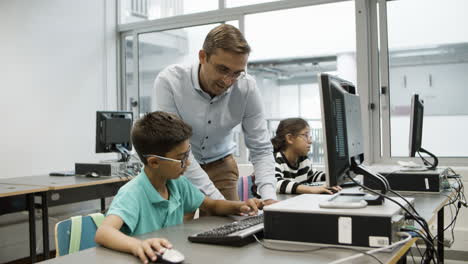 profesor sonriente y colegial trabajando juntos en la computadora