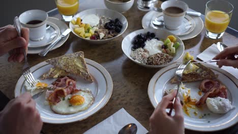 slowmo - hombre y mujer desayunando tocino y huevo, muesli casero, café y jugo de naranja en un hotel de lujo