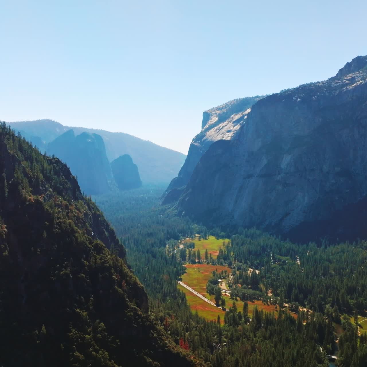 Green sunny valley among the cliff rocks of Yosemite National Park, California, United States. Aerial view at backdrop of clear skies