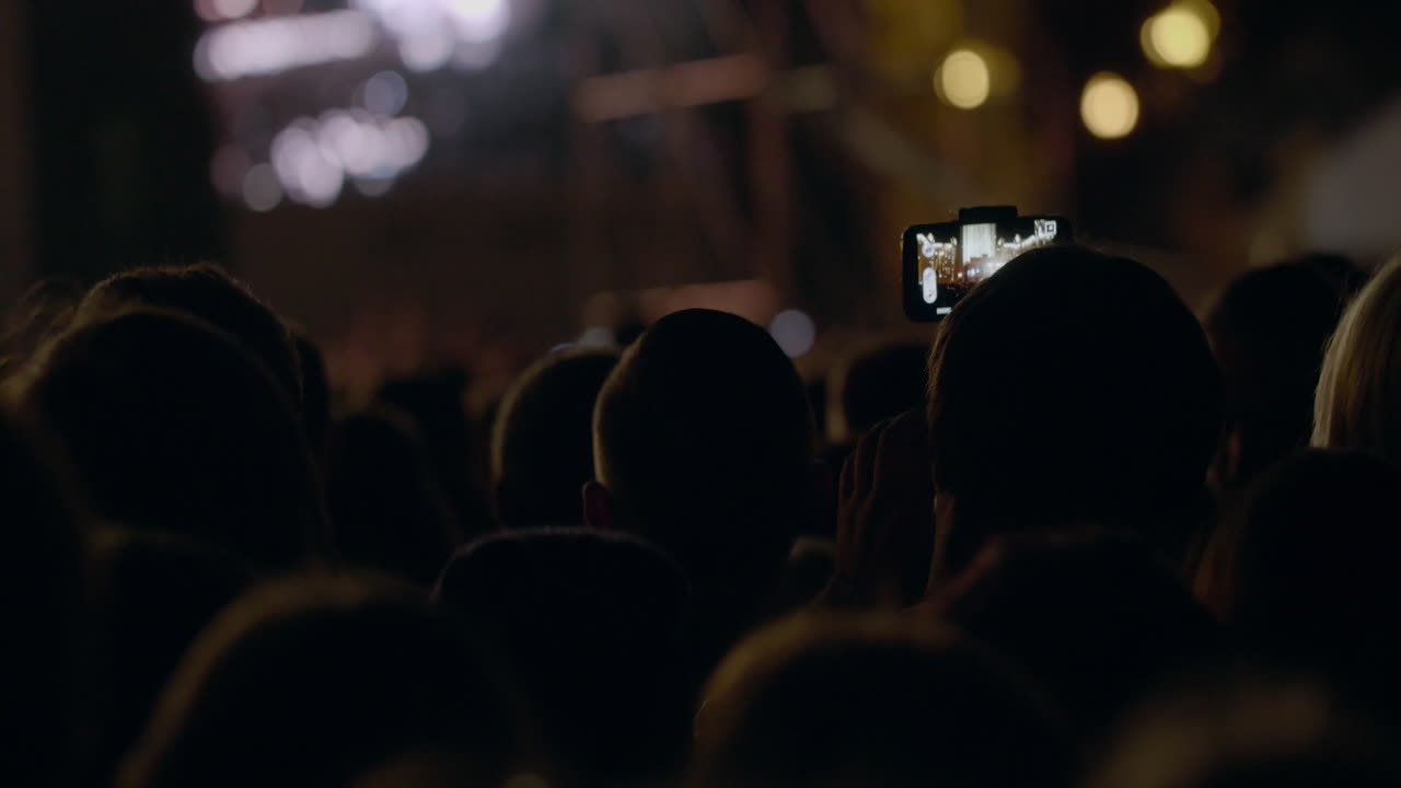 View From Behind Of Hands Hold Camera With Digital Display Among People 