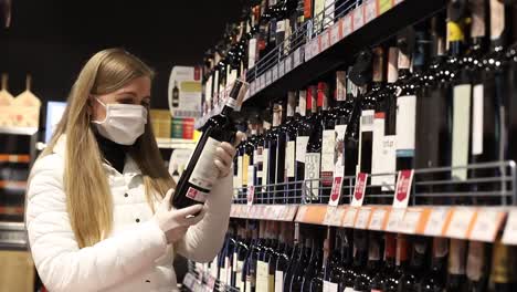 blonde in a medical mask chooses wine in the supermarket, buying food during the pandemic coronavirus