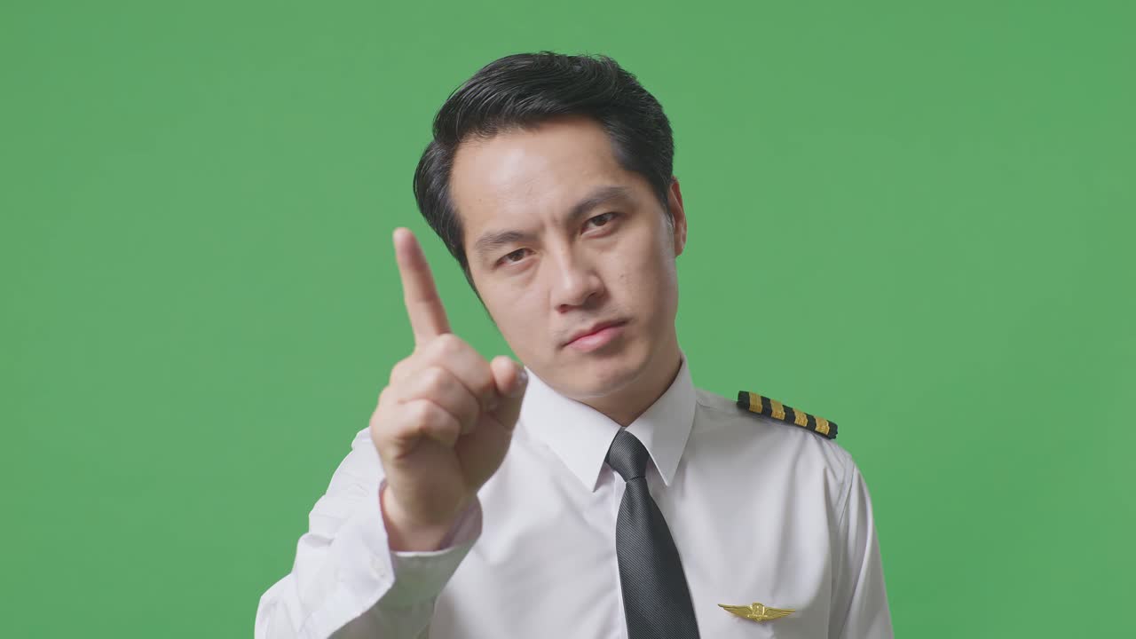 아시아 남성 조종사가 당신을 가리키고, 녹색 스크린 배경 스튜디오에서 지표손가락 표시 없이 불쾌감을 표합니다.