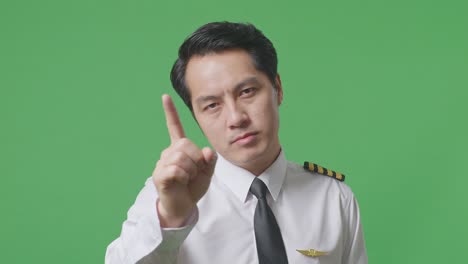 close up of asian man pilot pointing at you and disapproving with no index finger sign in the green screen background studio