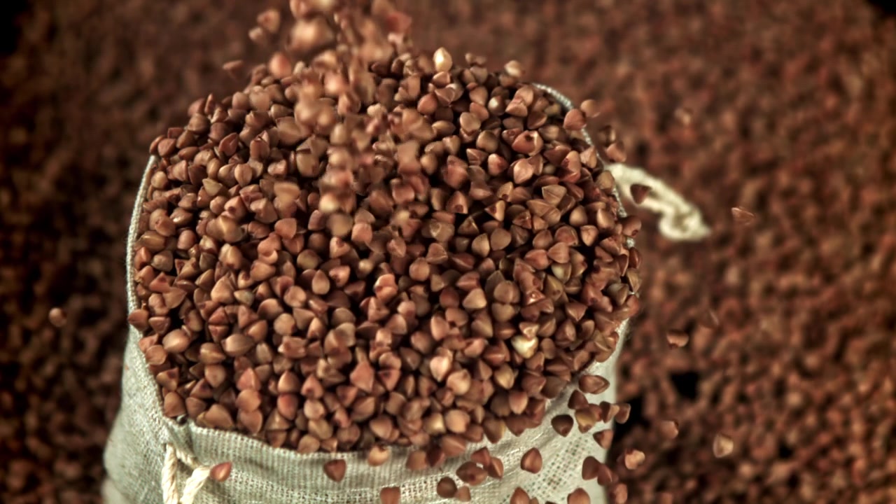 Chicchi di grano saraceno che si riversano e riempiono un sacco rustico