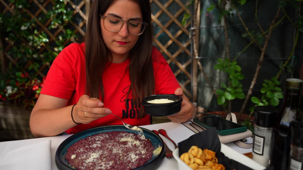 Young woman putting cheese on her Veronese dish of rice Risotto all'Amarone in Italian restaurant