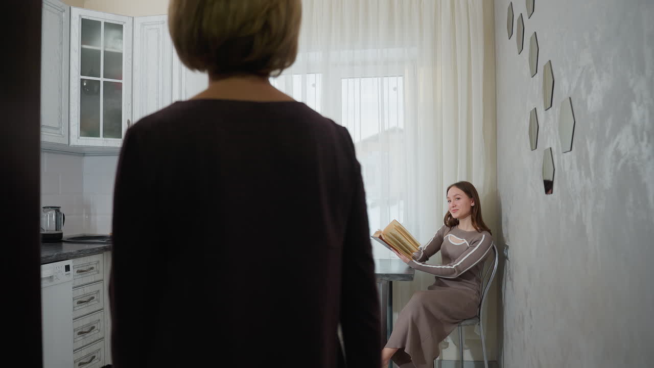 집주인은 딸과 함께 주방에 들어와 책상에 앉아 소설을 읽고, 딸은 엄마를 쳐다보고 따뜻하게 미소 짓고, 편안한 가정 환경에서 가 따뜻한 가족 순간을 불러일으킨다.