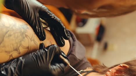 hands of tattooist in gloves injecting ink into skin with needle