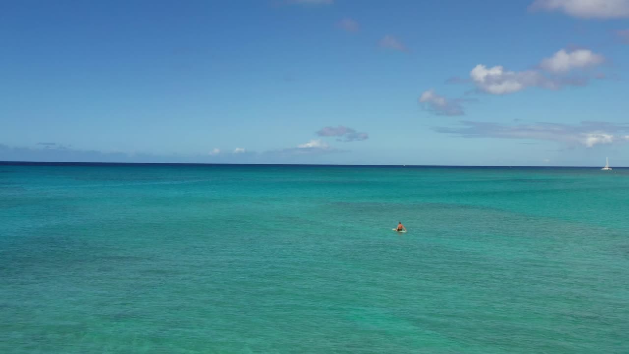Solitary swimmer floats in calm turquoise waters off Lanikai Beach, Oahu, Hawaii. A tranquil aerial scene of tropical clarity, open ocean, and peaceful solitude beneath a bright blue sky