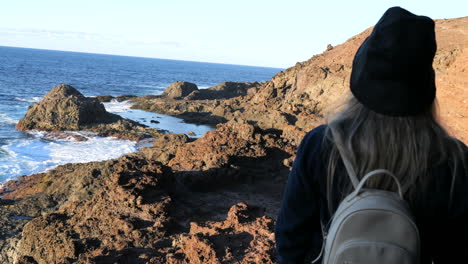 shot-of-a-young-woman-with-a-hat-admires-the-waves-of-the-coast-that-are-in-the-municipality-of-Galdar-on-the-island-of-Gran-Canaria-and-during-sunset