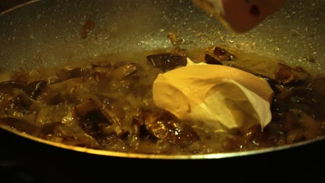 pouring sour cream to the pan full of frying mushrooms and mixing it