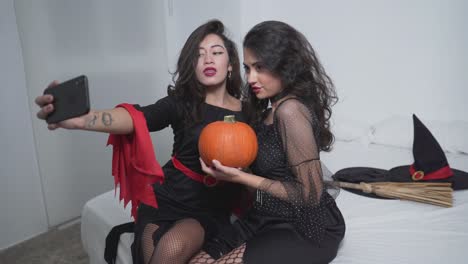 two witches taking a selfie with a pumpkin