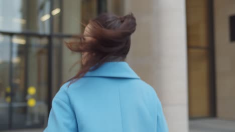 elegant young businesswoman in blue coat entering office building