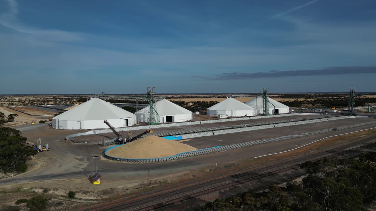 tomada aérea del drone que establece el centro de distribución industrial con montón de maíz y almacenamiento de silo durante un día soleado