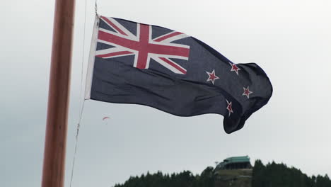 new zealand flag blowing in the queenstown wind with paraglider in the background