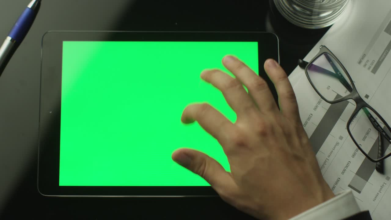 테이블 위에 누워있는 녹색 화면의 태블릿 pc를 사용하는 사업가.