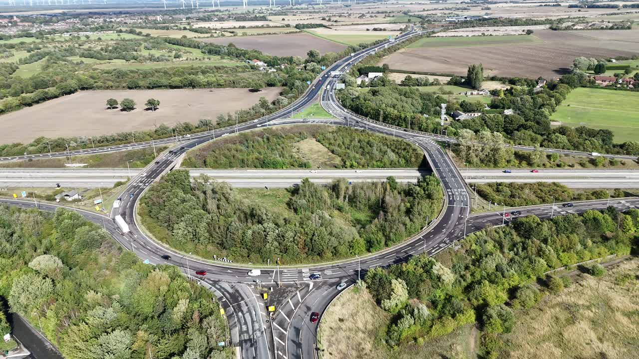 イギリス、ノースヨークシャーのディッシュフォース近郊にある主要な道路ジャンクションを映すドローン空撮映像。田園地帯、農地、樹木、高速道路、行き交う車両に囲まれている。
