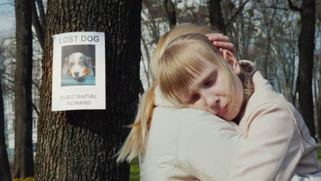 mom soothes the girl who lost the dog on the tree hangs the announcement of the missing puppy