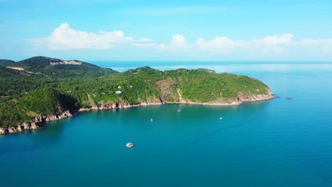 Rocky-coastline-of-tropical-island-with-lush-vegetation-surrounded-by-calm-blue-azure-sea-under-bright-sky-with-shiny-white-clouds-in-Vietnam