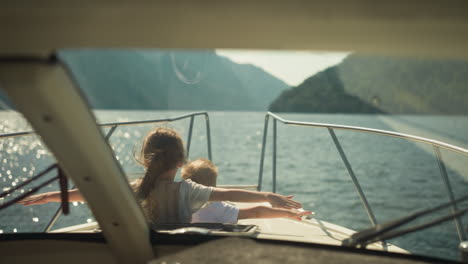 little children with outstretched arms lean out of cabin exit of motorboat in scenic sea. cheerful brother and sister sail yacht in ocean on summer holiday