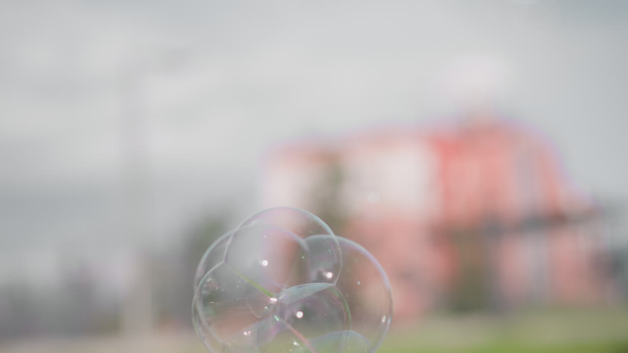 Primo piano di una donna di colore che soffia bolle di sapone iridescenti su un marciapiede urbano, riflessi delicati e scintillio, morbidi tocchi bokeh, una sola foglia sul cemento, atmosfera minimal serena e micro dettagli cinematografici