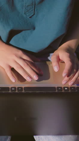 primer plano de una mujer usando una computadora portátil al aire libre por la noche, dedos escribiendo en el teclado con reflejo blanco en la pantalla, el fondo presenta un borrón suave