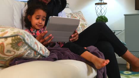 Young-mother-using-a-digital-tablet-with-her-daughter-on-the-sofa-at-home-4k