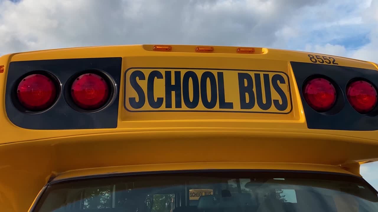 School bus close up circle right showing red lights in school parking lot; cropped