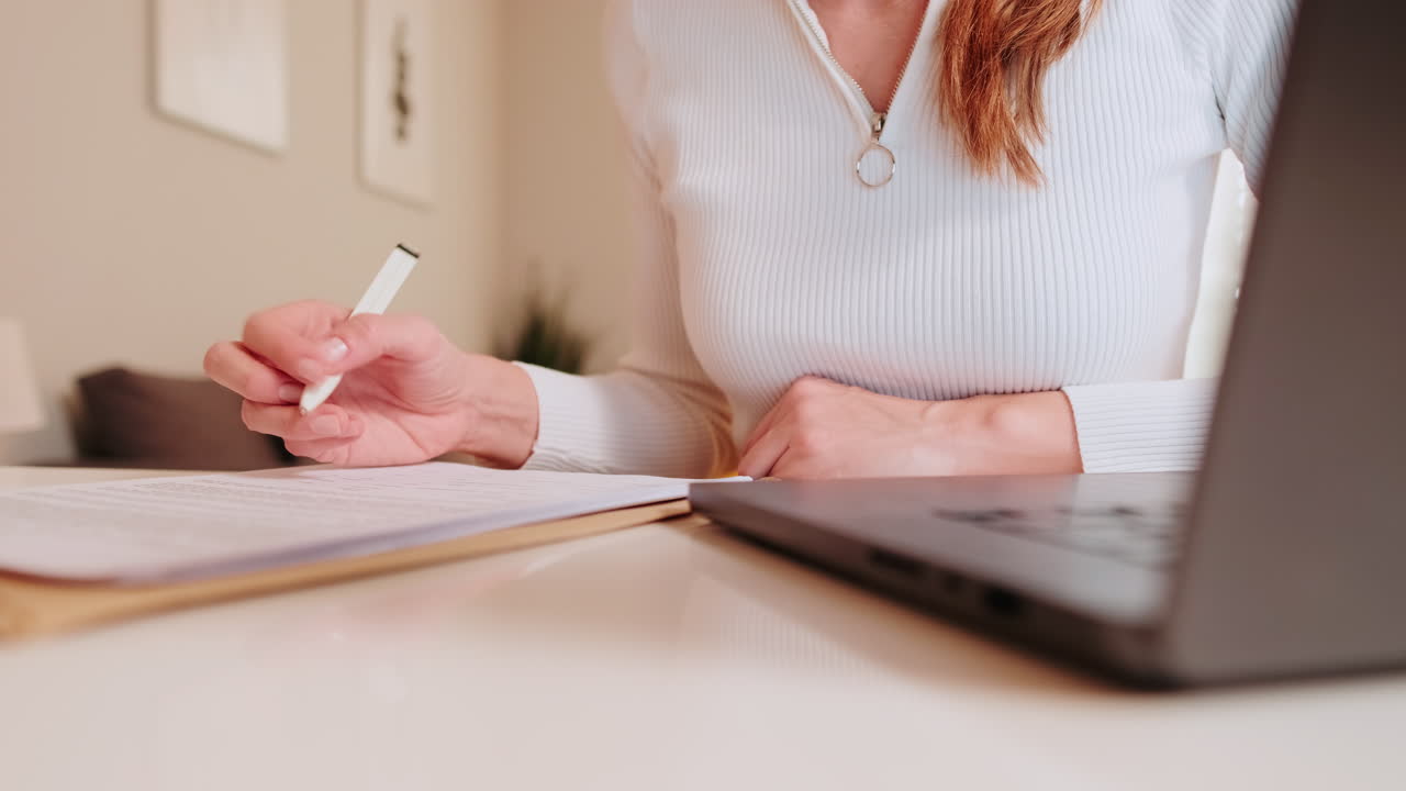 Donna che scrive su un documento alla scrivania con il laptop