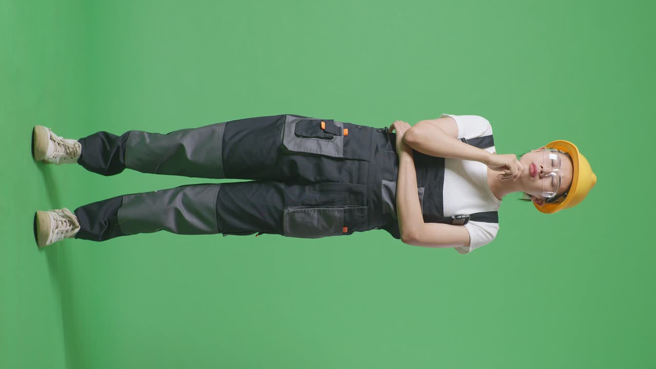 cuerpo lleno de trabajador mujer asiática con gafas de protección y casco de seguridad pensando en algo y mirando a su alrededor mientras está de pie en el estudio de fondo de la pantalla verde