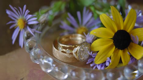 Hermosas-Alianzas-De-Boda-Planas-Con-Un-Plato-De-Cristal-Y-Hermosas-Flores-Amarillas-Y-Moradas