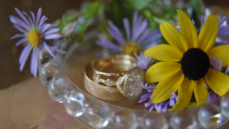 hermosas alianzas de boda planas con un plato de cristal y hermosas flores amarillas y moradas