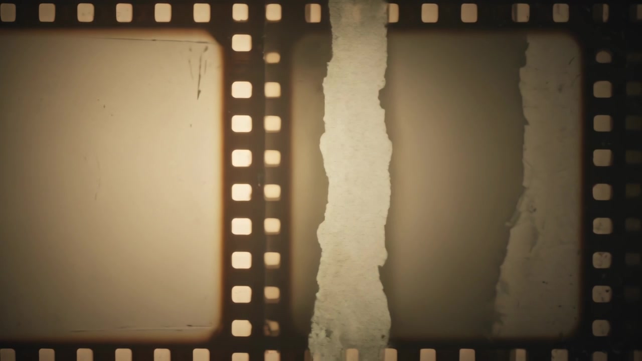 Striscia di pellicola da 35mm che avanza su un tavolo luminoso per la scansione, rivelando emulsione strappata e fori di trascinamento.