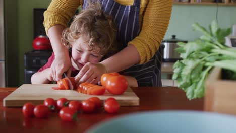 madre y hijo caucásicos felices cortando verduras en la cocina