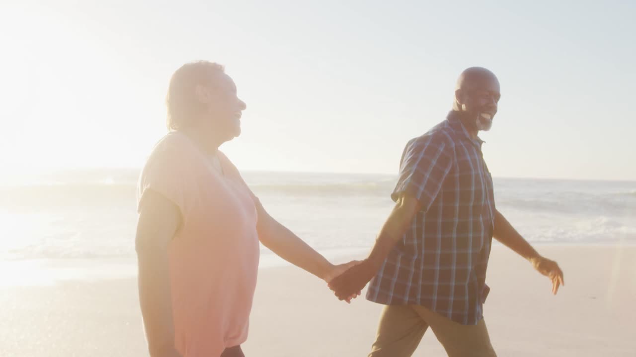 웃는 아프리카계 미국인 부부가 손을 잡고  ⁇ 은 해변에서  ⁇ 고 있습니다.