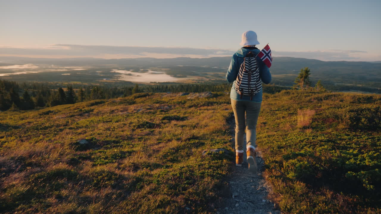 una mujer activa con una mochila y una bandera noruega está caminando por un sendero de montaña por delante es un im