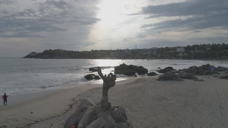 Aerial-shot-of-a-hand-statue-in-Zicatela-beach-at-sunset,-Puerto-Escondido,-Oaxaca