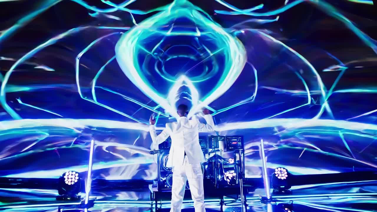Professional musician performing on stage, wearing white suit amid neon light projections during high energy electronic concert with dynamic visual design