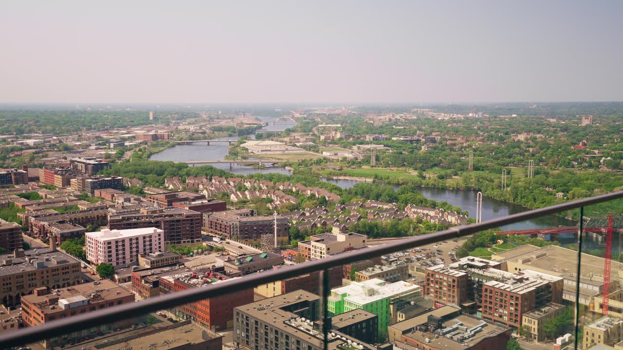 Overlooking shot from a high-rise building's railing, revealing a sprawling landscape of homes and a serene river in the distance