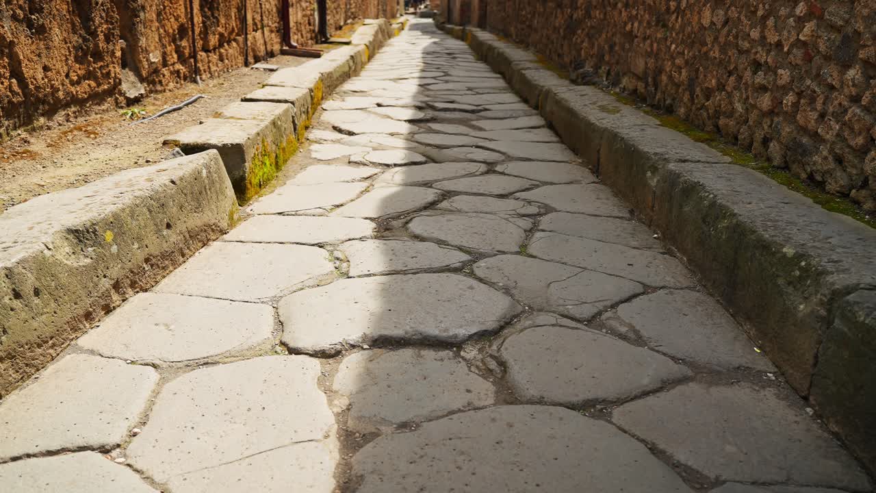 Vista a livello del suolo di una pavimentazione in pietra usurata a Pompei, che evidenzia la superficie stradale dell'antica Roma, i cordoli rialzati e la texture illuminata dal sole della strada archeologica